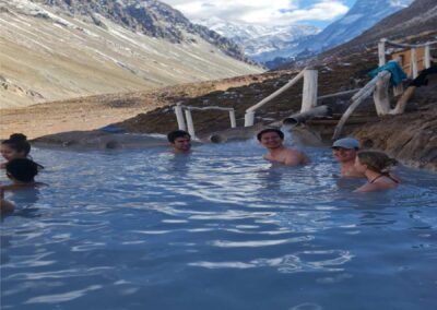 Grupo de personas disfrutando de los pozones termales de Termas de Colina, con el paisaje de la cordillera de fondo.