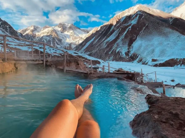 Persona relajándose en aguas termales frente a las montañas del Cajón del Maipo, parte del tour embalse el yeso y termas de colina.