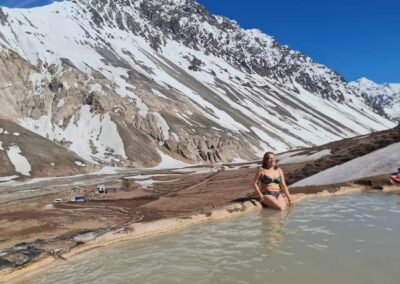 Persona disfrutando de los pozones termales de Termas de Colina, con una montaña nevada y cielo despejado de fondo.