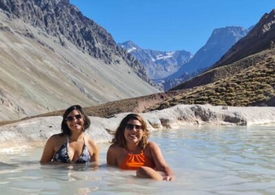 Dos turistas relajándose en las aguas termales de las Termas de Colina, con el paisaje cordillerano del Cajón del Maipo al fondo.