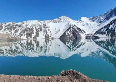 Vista panorámica del Embalse El Yeso con montañas nevadas reflejadas en el agua turquesa.