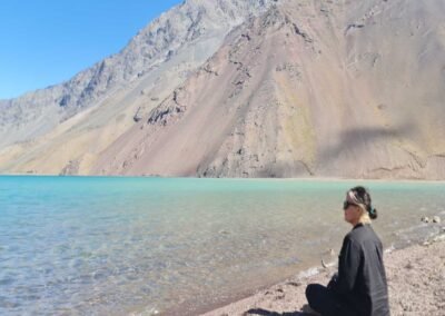 Persona sentada en una roca admirando el agua turquesa del Embalse El Yeso en verano.