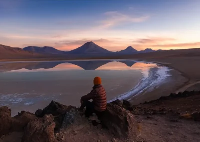 Persona sentada mirando una laguna altiplánica al atardecer en la zona del Volcán Láscar
